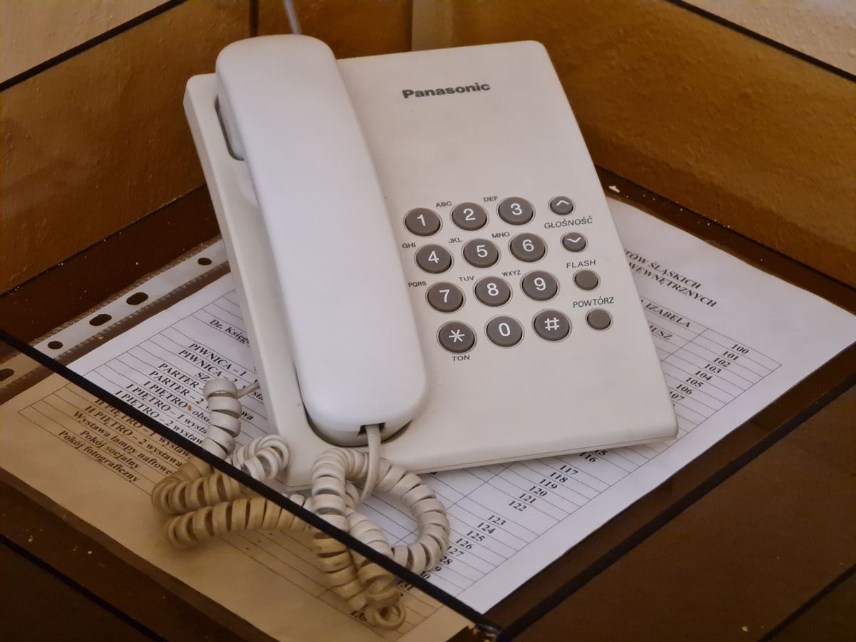 Téléphone fixe blanc à touches posé sur un bureau avec son cordon spiralé
